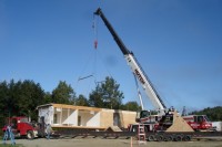 A photo of a construction crane installing a single-wide manufactured home.